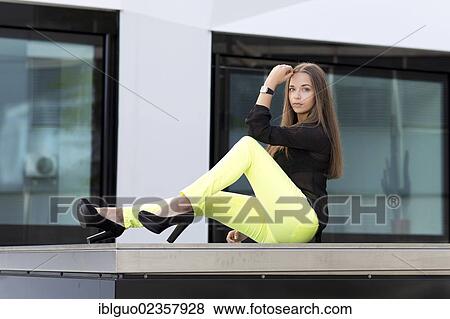 Stock Photo - "Young woman wearing a black top, bright yellow trousers and high black shoes". Fotosearch
