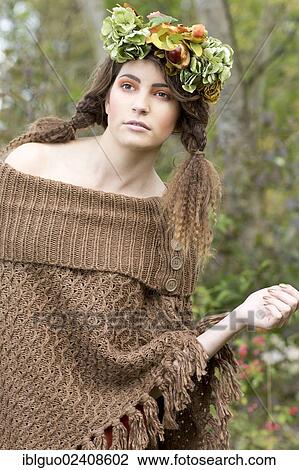 Stock Image - "Young woman wearing a brown poncho with a flowal wreath in her hair, outdoors". Fotosearch
