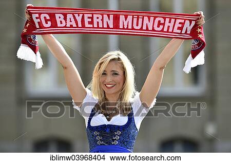 Picture - "Young woman wearing a dirndl, supporter of FC Bayern, holding up a fan scarf, Germany, Europe". Fotosearch