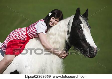 Stock Photo - "Young woman wearing a dirndl sitting without a saddle or bridle and cuddling with a Gypsy Vanner or Tinker horse, pinto, black and white, North Tyrol, Austria, Europe". Fotosearch