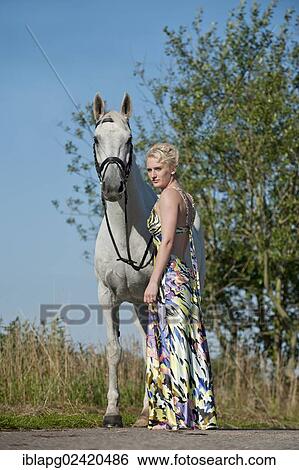 Stock Photograph - Young woman wearing a dress standing with a Hanoverian horse. Fotosearch