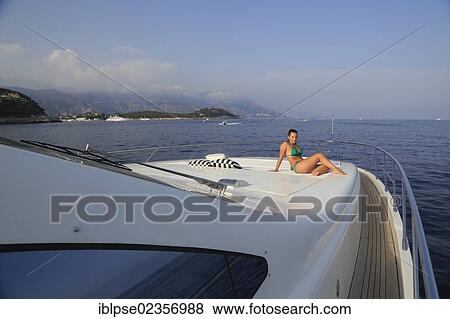 Stock Photo - "Young woman wearing a green bikini sitting on the front sun deck of a motor yacht, French Riviera, Cote d'Azur, Mediterranean Sea, Europe". Fotosearch