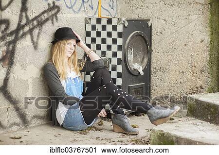 Stock Image - "Young woman wearing a hat posing in front of a wall with graffiti, Hesse, Germany, Europe". Fotosearch
