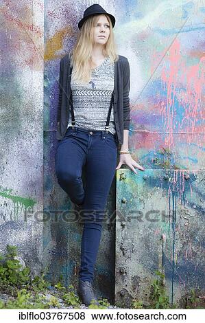 Stock Photo - "Young woman wearing a hat posing in front of a wall with graffiti, Hesse, Germany, Europe". Fotosearch
