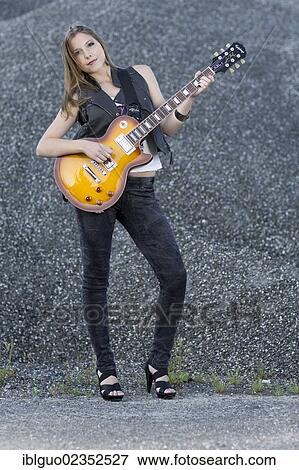 Young woman wearing a leather vest and jeans posing with an electric guitar View Large Photo Image Stock Photo - Young woman wearing a leather vest and jeans posing with an electric guitar. Fotosearch