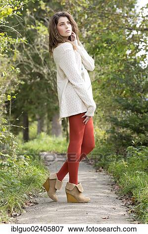 Stock Photo - "Young woman wearing a long white sweater and red tights, outdoors". Fotosearch