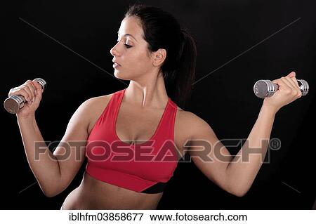 Stock Photo - "Young woman wearing a red sports bra holding mini dumbbells, training her arm muscles". Fotosearch
