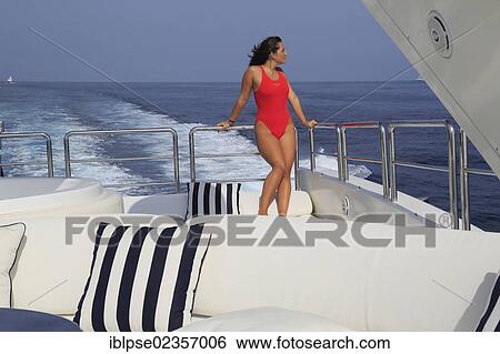Stock Photograph - "Young woman wearing a red swimsuit standing on the back deck of a moving motor yacht, French Riviera, Cote d'Azur, Mediterranean Sea, Europe". Fotosearch