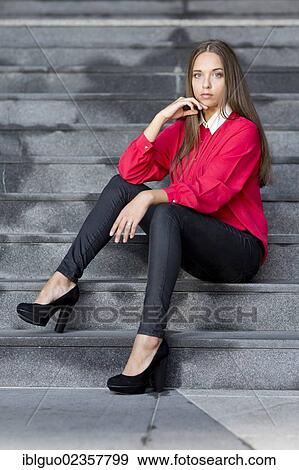 "Young woman wearing a red top, black trousers and high black shoes posing while sitting on stairs" View Large Photo Image Stock Photo - "Young woman wearing a red top, black trousers and high black shoes posing while sitting on stairs". Fotosearch