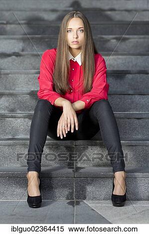 "Young woman wearing a red top, black jeans and high heels posing while sitting on stairs" View Large Photo Image Stock Photography - "Young woman wearing a red top, black jeans and high heels posing while sitting on stairs". Fotosearch