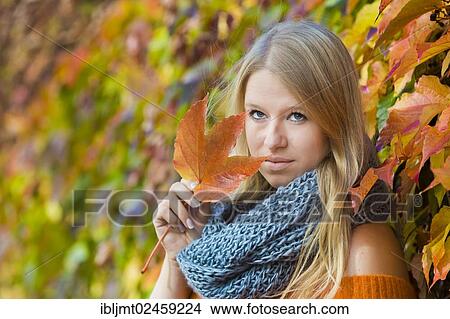 Young woman wearing a thick scarf and holding an autumnal coloured leaf in her hand View Large Photo Image Picture - Young woman wearing a thick scarf and holding an autumnal coloured leaf in her hand. Fotosearch