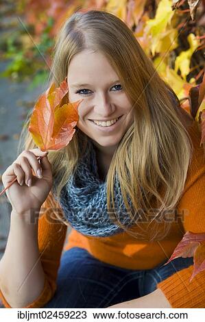 Young woman wearing a thick scarf and holding an autumnal coloured leaf in her hand View Large Photo Image Stock Image - Young woman wearing a thick scarf and holding an autumnal coloured leaf in her hand. Fotosearch