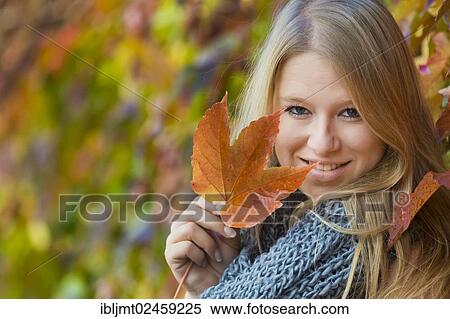 Young woman wearing a thick scarf and holding an autumnal coloured leaf in her hand View Large Photo Image Stock Photography - Young woman wearing a thick scarf and holding an autumnal coloured leaf in her hand. Fotosearch