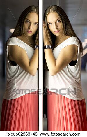 Stock Image - "Young woman wearing a white top and a red skirt, mirror image". Fotosearch