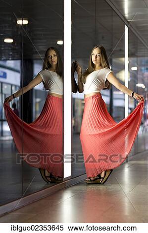 Young woman wearing a white top and a long red dress in front of a wall of mirrors with her mirrored image View Large Photo Image Stock Photography - Young woman wearing a white top and a long red dress in front of a wall of mirrors with her mirrored image. Fotosearch