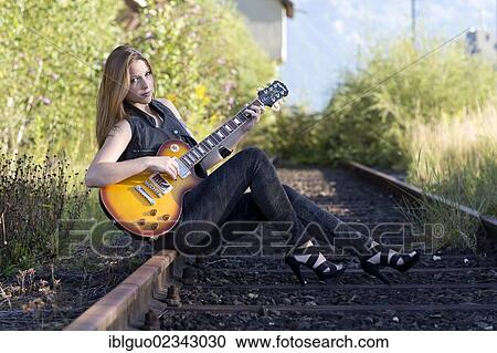 Young woman wearing dark jeans and high heels sitting with an electric guitar on a railway track View Large Photo Image Stock Image - Young woman wearing dark jeans and high heels sitting with an electric guitar on a railway track. Fotosearch