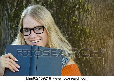 Stock Photo - Young woman wearing glasses looking over the edge of a book. Fotosearch