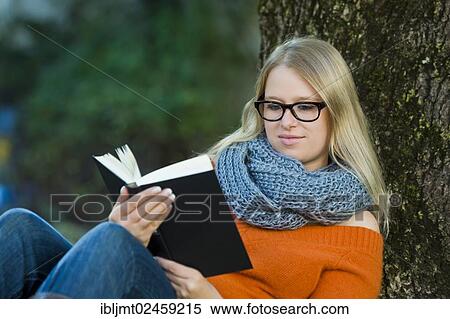 Stock Photography - Young woman wearing glasses sitting in the park and reading a book. Fotosearch