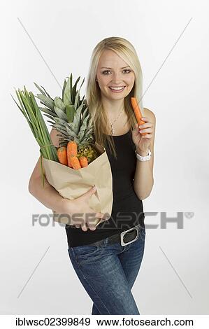"Young woman with a bag full of vegetables and fruit in her arm, holding a carrot in her hand" View Large Photo Image Stock Photo - "Young woman with a bag full of vegetables and fruit in her arm, holding a carrot in her hand". Fotosearch