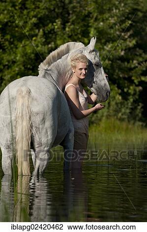 Stock Image - Young woman with a Hanoverian horse in a lake. Fotosearch