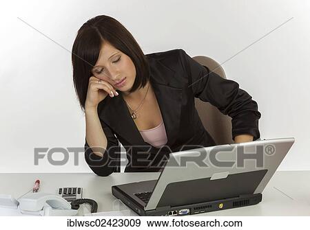 Stock Photo - Young woman with a laptop sitting at a desk and sleeping. Fotosearch