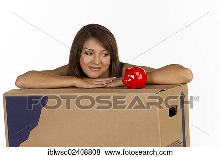 Stock Photo - Young woman with a moving box and a piggy bank. Fotosearch