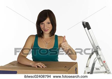 "Young woman with a moving box, making a thumbs-up gesture" View Large Photo Image Picture - "Young woman with a moving box, making a thumbs-up gesture". Fotosearch