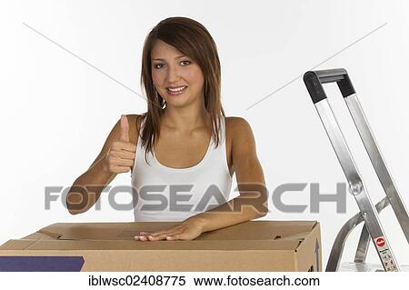 "Young woman with a moving box, making a thumbs-up gesture" View Large Photo Image Stock Photography - "Young woman with a moving box, making a thumbs-up gesture". Fotosearch