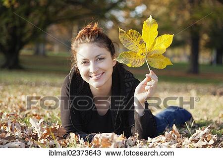 Stock Image - Young woman with an autumn leaf in her hand on a meadow. Fotosearch