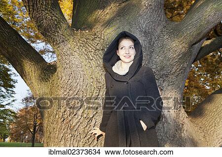 Young woman with hooded coat next to a tree View Large Photo Image Picture - Young woman with hooded coat next to a tree. Fotosearch