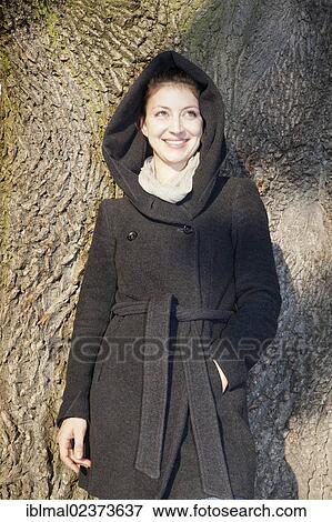 Young woman with hooded coat next to a tree View Large Photo Image Stock Photo - Young woman with hooded coat next to a tree. Fotosearch