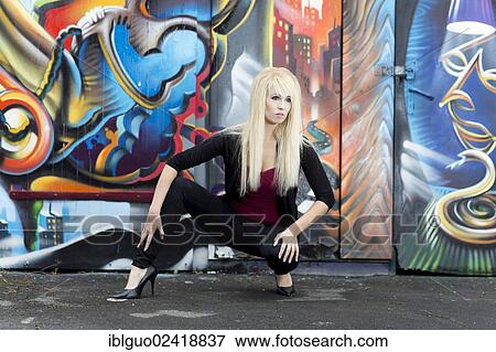 Stock Photo - Young woman with long blonde hair posing in front of a wall with graffiti. Fotosearch
