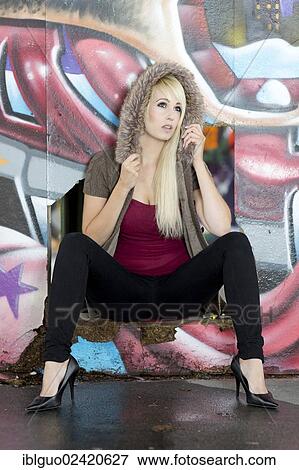 Young woman with long blonde hair posing in front of a wall with graffiti View Large Photo Image Stock Photo - Young woman with long blonde hair posing in front of a wall with graffiti. Fotosearch
