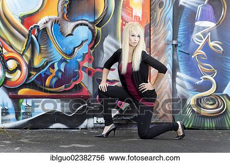 Stock Photograph - Young woman with long blonde hair posing in front of a wall with graffiti. Fotosearch