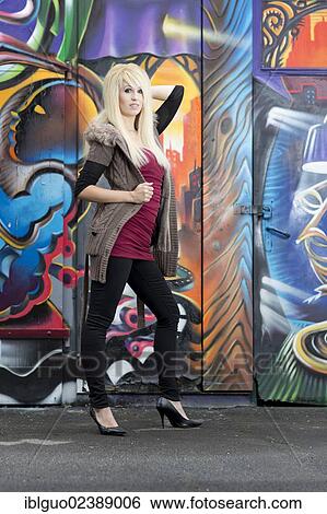 Stock Photograph - Young woman with long blonde hair posing in front of a wall with graffiti. Fotosearch