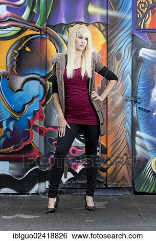 Stock Photograph - Young woman with long blonde hair posing in front of a wall with graffiti. Fotosearch