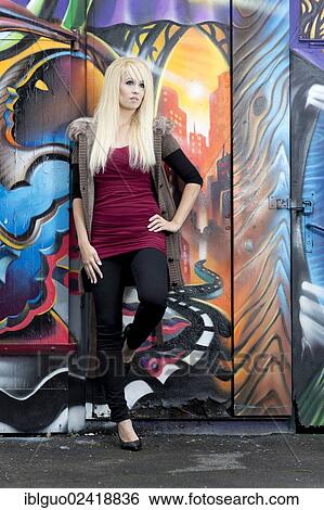 Stock Photograph - Young woman with long blonde hair posing in front of a wall with graffiti. Fotosearch