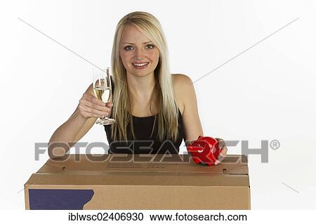 Stock Image - "Young woman with moving box, glass of champagne and piggy bank". Fotosearch