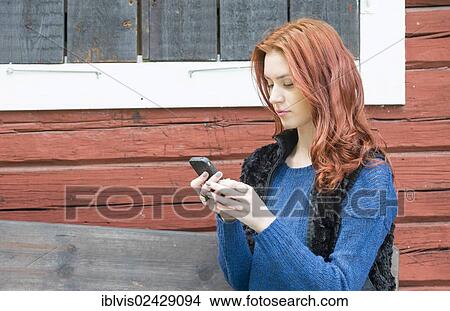 Young woman with red hair looking at a message on her smartphone View Large Photo Image Picture - Young woman with red hair looking at a message on her smartphone. Fotosearch