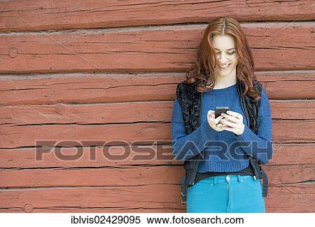 Young woman with red hair smiling and looking at her mobile phone View Large Photo Image Stock Photography - Young woman with red hair smiling and looking at her mobile phone. Fotosearch