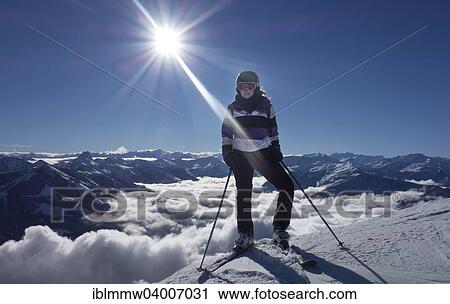 Stock Image - "Young woman with ski equipment against Alps mountains, Austria, Europe". Fotosearch