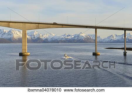 Stock Image - Boat at the Hadsel bridge, behind the snow-capped peaks of Hinnoya island, Langoysund in Stokmarknes, Nordland, Vesteralen, Norway, Europe. Fotosearch