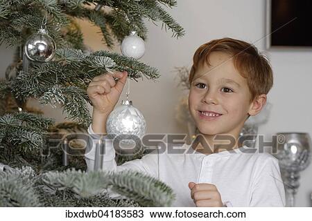 Stock Image - Boy decorating a Christmas tree with baubles, Bavaria, Germany, Europe. Fotosearch