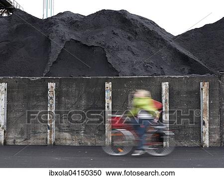 Stock Image - Cyclist riding past coal ash heap, Offenbach, Hesse, Germany, Europe. Fotosearch