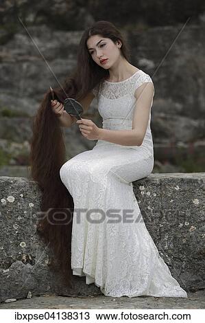 Stock Image - Enactment of the painting Lady Lilith by Dante Gabriel Rossetti, young woman in a white dress, combing her hair and looking in the mirror. Fotosearch