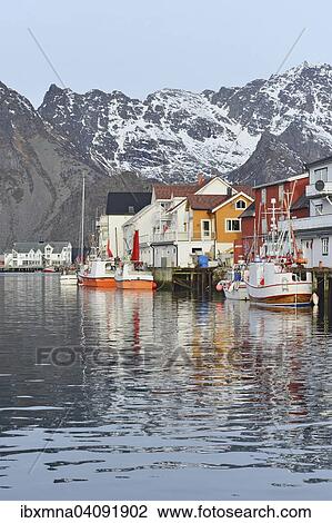 Stock Image - Fishing village with boats in the harbor in front of snow-capped mountains of the island Austvagoy, Henningsvaer, Lofoten, Nordland, Norway, Europe. Fotosearch