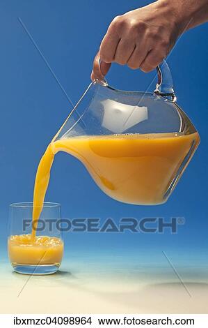 Hand pouring orange juice out of a jug into a glass View Large Photo Image Picture - Hand pouring orange juice out of a jug into a glass. Fotosearch