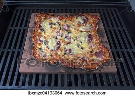 Homemade Pizza Speziale, tomatoes, cooked ham, salami and cheese on a hot stone in a gas grill View Large Photo Image Picture - Homemade Pizza Speziale, tomatoes, cooked ham, salami and cheese on a hot stone in a gas grill. Fotosearch