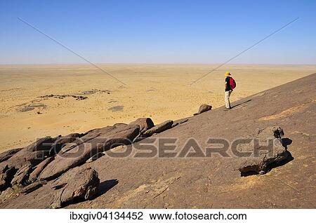 Stock Image - Man looking from Aicha monolith towards the flat desert, Adrar region, Mauritania, Africa. Fotosearch