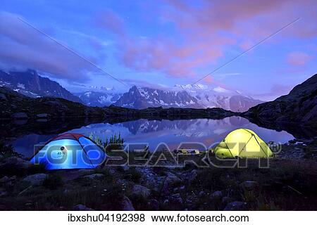 Stock Photo - Mont Blanc massif at night reflected in Lac de Chesserys, two lighted tents at the front, Chamonix, France, Europe. Fotosearch